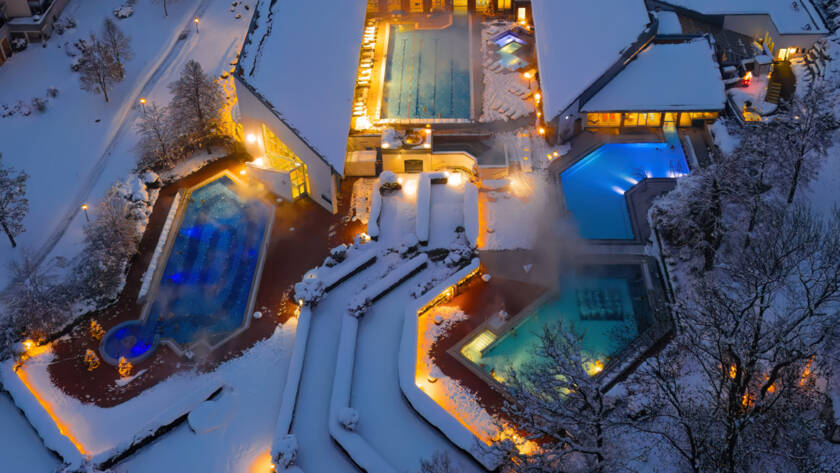 Winterliche Drohnenaufnahme am Abend mit weihnachtlicher Beleuchtung und farbig beleuchteten Becken.