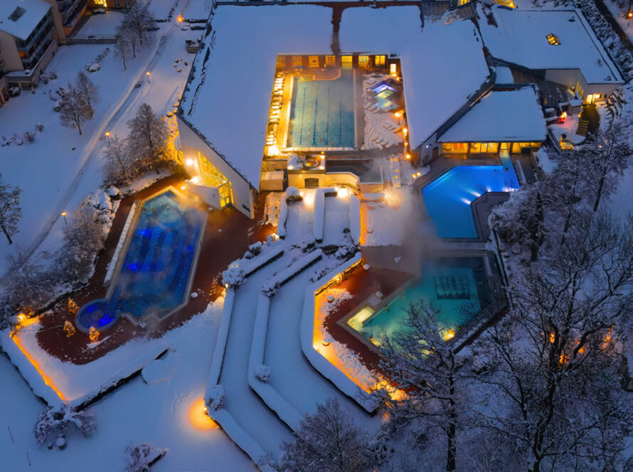 Winterliche Drohnenaufnahme am Abend mit weihnachtlicher Beleuchtung und farbig beleuchteten Becken.