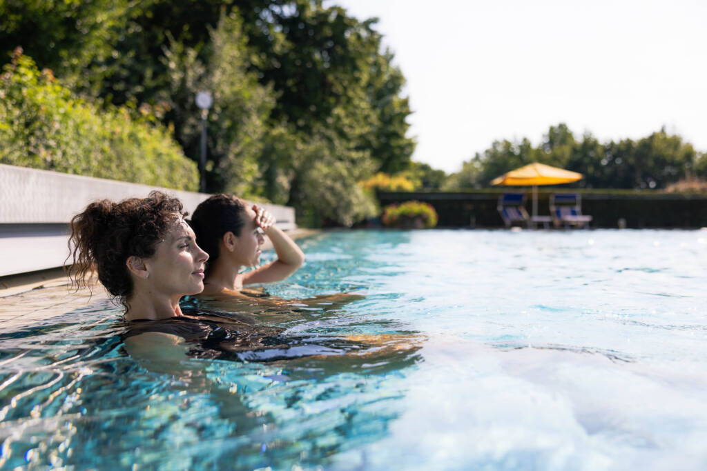 Zwei Frauen genießen die Sonne im Außenbecken der Wohlfühl-Therme Bad Griesbach, im Hintergrund ist ein gelber Sonnenschirm zu sehen.